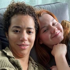 two women are laying down on a couch smiling at the camera and one is holding her arm around the other woman's shoulder