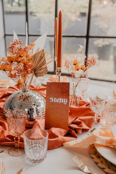 the table is set with orange napkins, silverware and an elegant centerpiece