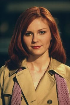 a woman with red hair and blue eyes wearing a trench coat is looking at the camera