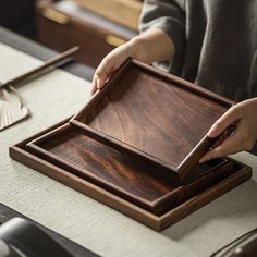 a person holding a wooden tray on top of a table