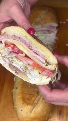 a person holding a sandwich in their hand on top of a wooden table next to bread