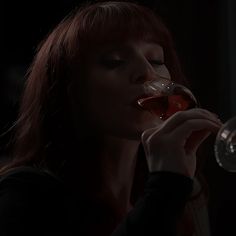 a woman drinking from a wine glass in the dark