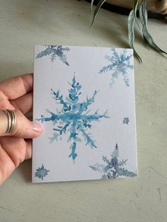 a hand holding up a card with blue snowflakes on it and a plant in the background