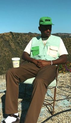 a man sitting in a chair on top of a hill with a cup of coffee