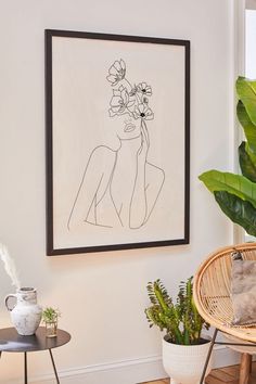 a drawing hangs on the wall next to a wicker chair and potted plant