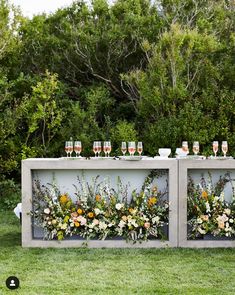 an outdoor bar with flowers and wine glasses on it's side, surrounded by greenery