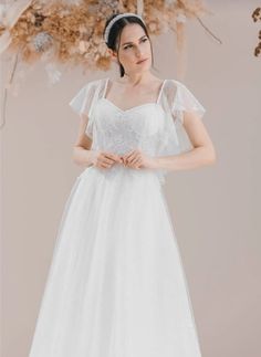 a woman in a white wedding dress standing next to a floral arrangement with flowers on it