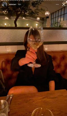 a woman sitting at a table with a wine glass in front of her face,