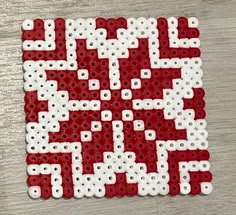 a piece of art made out of white and red beads on a wooden surface with the word qr code printed on it