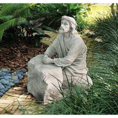 a statue of jesus sitting on a rock in the middle of some plants and rocks