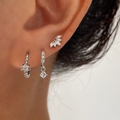 a woman's ear is adorned with three small white cubics and two smaller diamond earrings