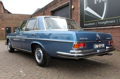 an old blue car parked in front of a brick building