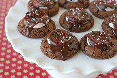 chocolate cookies with white and red sprinkles are on a plate next to a spoon