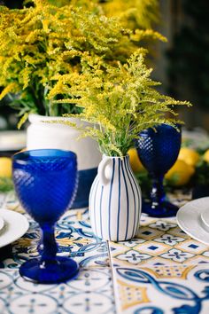 blue and white vases with yellow flowers in them on a dining table set for two