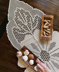 a person holding a plate with small shells on it next to a doily and wooden tray