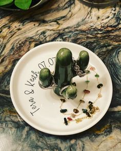 a white plate topped with two green cactus plants and some other jewelry on top of it