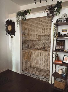 a room with a shelf, clock and plants on the wall next to an open door