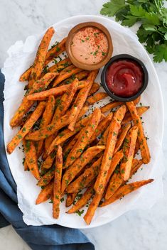 baked sweet potato fries with ketchup and parsley on a white platter