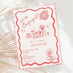 a red and white wedding card with the words we're engaged on it next to some paper fans