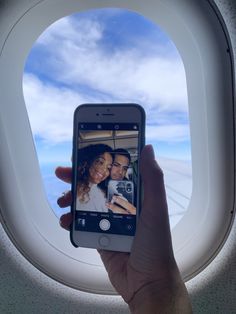 a person holding up a cell phone to take a selfie in front of an airplane window