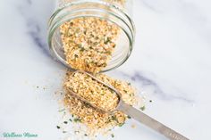 a jar filled with granola next to a spoon on top of a marble counter