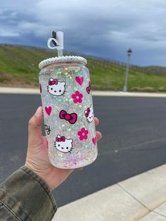 a person holding up a hello kitty water bottle with hearts and flowers on the lid