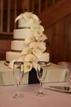 two wine glasses sitting on top of a table next to a wedding cake with white flowers