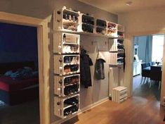 an open closet with shoes and clothes hanging on the wall next to a bed in a living room