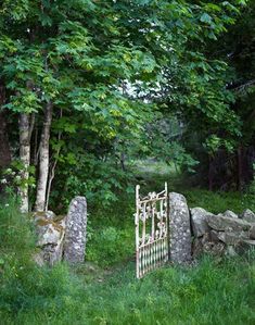 an old stone gate in the middle of a grassy area surrounded by trees and rocks