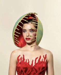 a woman in a red dress and green hat with gold accents on her face, standing against a beige background