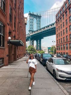 a woman is walking down the sidewalk in front of some tall buildings and a bridge