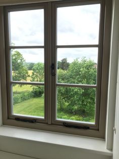 an open window in a white room with trees outside the window and grass below it