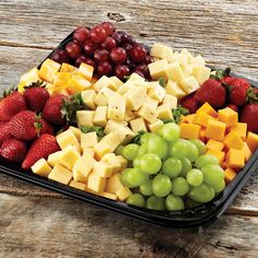 grapes, strawberries, and cheese are arranged in a tray on a wooden table