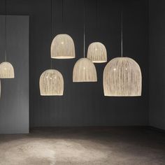 five hanging lights in an empty room with concrete flooring and dark walls behind them