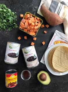 ingredients to make sweet potato tortillas laid out on a black table with avocado, carrots and other foodstuffs