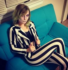 a woman sitting on top of a blue couch wearing black and white striped pants with her legs crossed