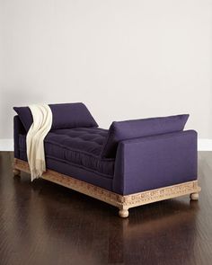 a purple couch sitting on top of a hard wood floor next to a white wall