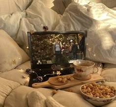 an open laptop computer sitting on top of a bed next to a bowl of food