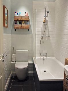 a white toilet sitting next to a bath tub under a bathroom mirror with shelves above it