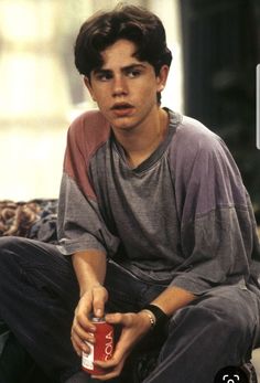 a young man sitting on the ground holding a can