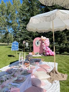 an outdoor table set up with pink and white plates, napkins, and umbrella