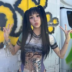 a woman with long black hair standing in front of a wall holding up two fingers