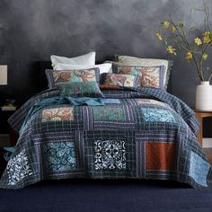 a bed covered in a blue and brown quilt next to a vase with yellow flowers