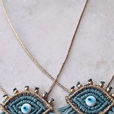 two necklaces with blue beads and gold chains on a marble surface, one has an evil eye in the center