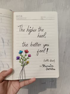 a hand holding an open notebook with writing on it and flowers in the bottom right corner