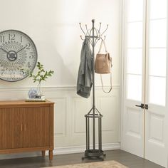 a coat rack with two coats hanging from it's sides and a clock on the wall behind it