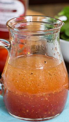 a glass pitcher filled with liquid sitting on top of a blue table cloth next to tomatoes and lettuce