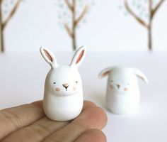 a hand holding a small white rabbit figurine in front of two smaller ones