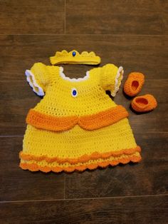 a crocheted baby dress and booties are laying on the floor