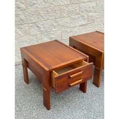 two wooden tables sitting next to each other on top of a cement ground near a brick wall